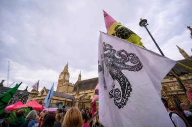 LONDON - 22 Nisan 2023: XR protesto yürüyüşüne katılın ve parlamentonun sembolik binaları yakınlarındaki protestocuların üzerinde dalgalanan bayrakların etkili görüntüsüne tanık olun..