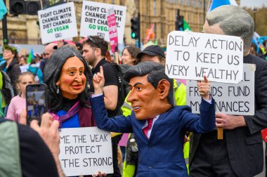 LONDON - 22 Nisan 2023 XR protestocuları Rishi Sunak ve eşi Akshata Murty 'nin dev maskeli maskelerini takarken, Soyu Tükenme İsyanı yürüyüşünde iklim protestosu işaretleri tutuyorlardı..