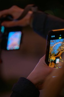 22 Nisan 2023: Bir el cep telefonunu tutuyor, ağaçlardaki turuncu ışıkları çerçeveliyor ve Londra Gözü, Stephen Lawrence Günü akşamında dokunaklı bir övgü..