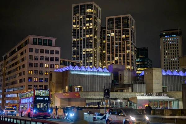LONDON - 22 Nisan 2023 Londra hareket halinde: gece Hayward Galerisi ve şehir daireleri tarafından çerçevelenmiş Waterloo Köprüsü 'nden geçen ikonik kırmızı otobüse tanık olun.