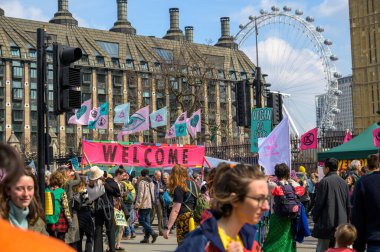 LONDON - 22 Nisan 2023: Birleştirici görseller: Söndürme İsyanı protestocuları, havada bayraklar, iklim hareketi çağrısını sembolize eden ikonik Londra Gözü 'nün önünde durun. Arkaplanda Kabuk Merkezi Binası.