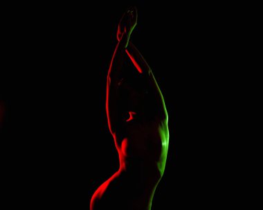 Renkli ışıklarda çıplak kadın silueti. Karanlık stüdyoda zarif seksi poz veren kız.