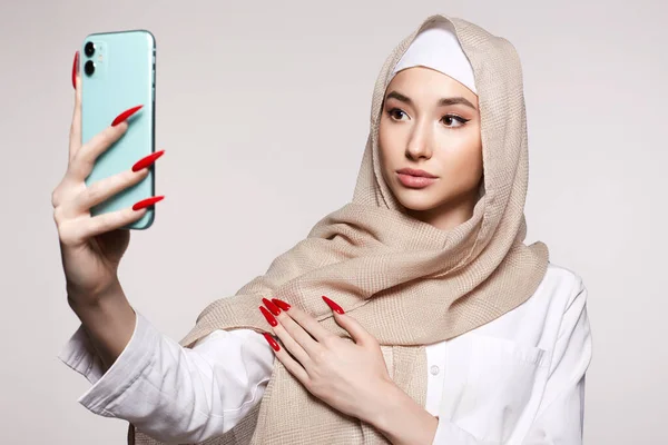 スマートフォンを持つ美しいイスラム教徒の若い女性が自撮りをしています ヒジャーブの美少女が画面を見てる ファッションオリエンタルスタイルモデル アジアの顔 — ストック写真