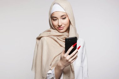 Akıllı telefonlu güzel, gülümseyen bir İslami genç kadın. Güzel tesettürlü mutlu kız ekrana bakıyor. Moda doğulu modeli. Asyalı yüzü