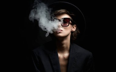 Güneş gözlüklü ve şapkalı güzel bir kadın. Takım elbiseli güzel bayan ağzından duman salıyor.