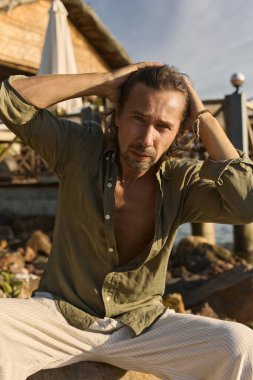 stylish boy at sunset. handsome long hair man is sitting in nature. Summer Fashion