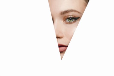 Beyaz üçgendeki genç ve güzel kadın. Makyöz konsepti. Parlak gölgeli, güzel yeşil gözleri olan bir kız beyaz kağıt deliğine bakar.