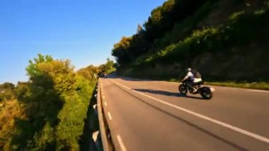 Dynamic fpv drone shot chasing Motorcycle driving under the bridge while sunset on serpentine road during golden hour, driver with white long sleeve shirt . followed with high speed fpv drone, 4k