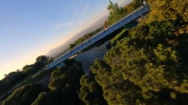Dynamic fpv drone shot chasing Motorcycle driving under the bridge while sunset on serpentine road during golden hour, driver with white long sleeve shirt . followed with high speed fpv drone, 4k