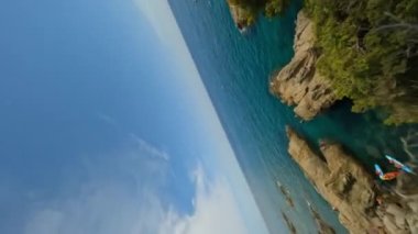 Vertically orientated Dynamic fpv shot down the cliff catching a guy jumping in to water from a Rock, Costa Brava In Spain, Catalonia Aerial view. High quality 4k footage
