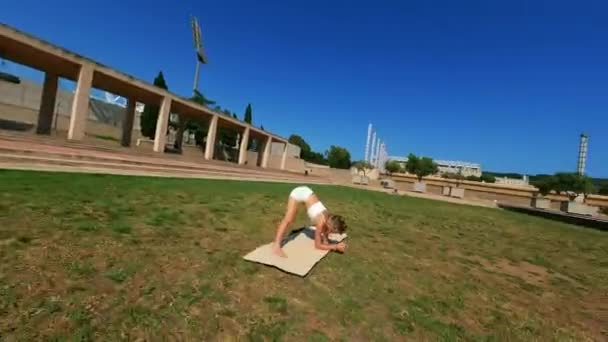 白衣姿の少女を飛び回るダイナミックなFpvドローンは 晴れた日に草の上でストレッチ演習を行い マットを使用して撮影しました 高品質4K映像 — ストック動画