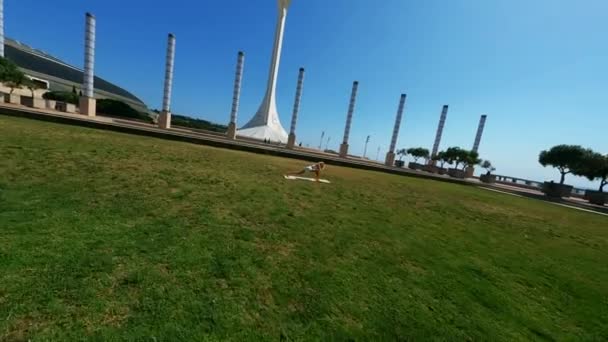 白衣姿の少女を飛び回るダイナミックなFpvドローンは 晴れた日に草の上でストレッチ演習を行い マットを使用して撮影しました 高品質4K映像 — ストック動画