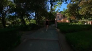 Spor siyah elbiseli kızı takip eden dinamik FPV hava aracı merdiveni çıkıyor. Güneşli bir günde, açık hava parkındaki eski mimari bina. Yüksek kalite 4k görüntü
