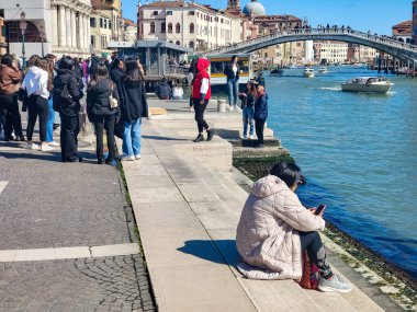 Venedik, İtalya - Nisan 2023. Yelkenli Venedik kanalları ve güneşli bir günde sokaklarda yürüyen turistler.