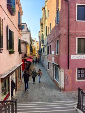 Venedik, İtalya - Nisan 2023. Güneşli bir günde Venedik sokaklarında yürüyen bir turist..