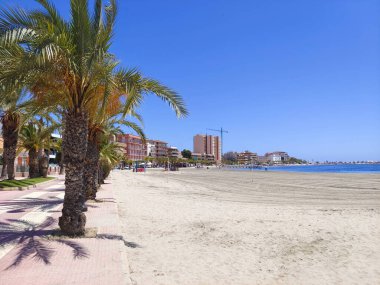 San Javier, Murcia, Spain - Jun, 10, 2022. Tourists in the beach of La Manga del Mar Menor with palm trees. Its a sunny day in the mediterranean sea. clipart