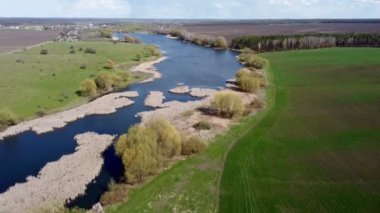 Drone footage of a river in a field. Blue river, reeds, trees and fields around. Beautiful landscape during the day against the blue sky.