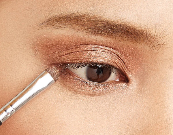Close up of eye makeup with brown shimmer eyeshadow applied using a blending brush. Beauty detail showing professional eye makeup application, soft glam style, and cosmetic technique.
