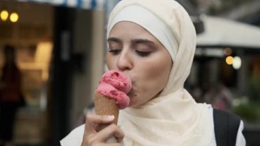 Genç bir Arap kadının tesettüre yakın çekilişi. Sokakta dururken dondurma yemekten zevk alıyor..