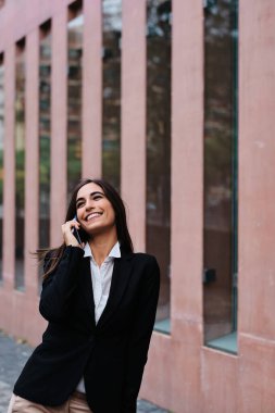 Havalı bir iş kadınının caddedeki cep telefonuyla konuştuğu dikey fotoğraf.