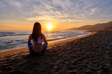 Tanımlanamayan fit bir kadının kumsalda gün batımını seyredişinin arka görüntüsü.