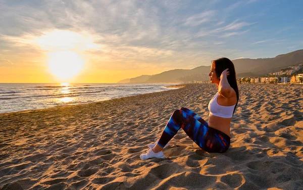 Stock image Profile of a caucasian fit woman doing abs on a beach during sunset