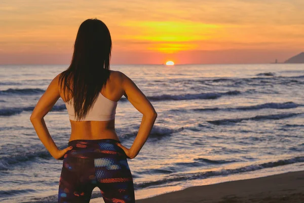 ビーチで夕日に直面しながら立っているスポーティなフィット原因アジアの女性の背面ビュー — ストック写真
