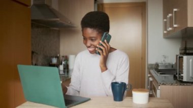 Evde kahve içerken dizüstü bilgisayarla çalışan neşeli siyahi bir kadının yavaş çekim videosu.