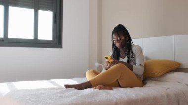 Vitiligo 'lu mutlu bir Afrikalı kadının yatakta otururken cep telefonunu kullanırken gülüşünün yavaş çekim videosu.