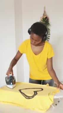 Kafası karışık bir Afrikalı kadının evde ütü yaparken müzik dinlediği dikey yavaş çekim videosu.