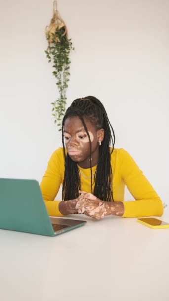 低速の動き垂直ビデオの心配黒女性とともにVitiligo肌の状態ジェスチャーで絶望で仕事中にノートパソコンでホーム — ストック動画