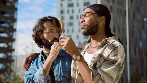 慢镜头 一对多元文化的同性恋夫妇一边在街上吃着甜棒棒糖一边欣赏 — 图库视频影像