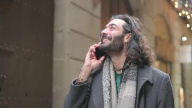 Şehir caddesinde cep telefonuyla konuşurken gülümseyen bir yetişkinin yavaş çekim videosu.