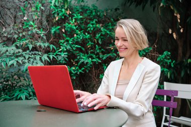 İş kadını dışarıda bir masada dizüstü bilgisayarla çalışırken gülümsüyor. İş ve teknoloji kavramı.