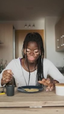 Vitiligo 'lu bir Afrikalı kadının evde kahvaltı yaparken konuşmasının yavaş çekim dikey videosu.