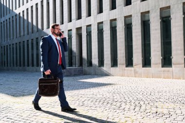 Sokakta yürürken cep telefonuyla konuşan bir işadamının fotokopi çekilen yatay fotoğrafı.