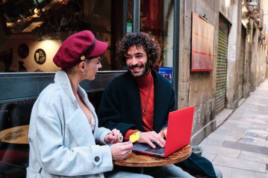 İnternetten alışveriş yapan şık bir çift sokakta bir kafeteryanın terasında oturuyor.