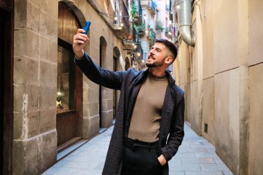 Şehirde selfie çekerken gülümseyen yakışıklı bir adamın portresi.