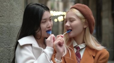 Sokakta flört ederken lolipop yiyen Asyalı lezbiyen bir çiftin yavaş çekim videosu.