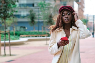 Sokakta elinde cep telefonu olan şık bir kadın kameraya bakıyor. Teknoloji konsepti.