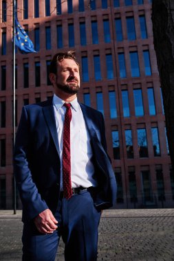 Avrupa bayrağı olan bir binanın yanındaki güçlü bir iş adamının kütük açılı fotoğrafı.