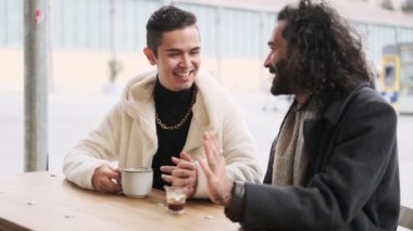 Açık hava kafeteryasında kahve içerken gay bir çiftin kucaklaşmasının yavaş çekim videosu.