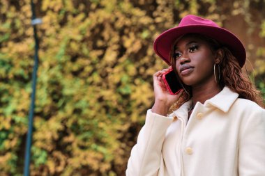 Stylish woman in a coat and hat talking on the phone while standing outdoors. Technology and communication concept.