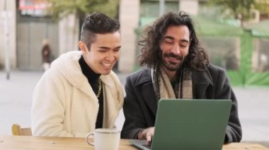 Slow motion video of a happy gay couple using a laptop sitting in a cafeteria