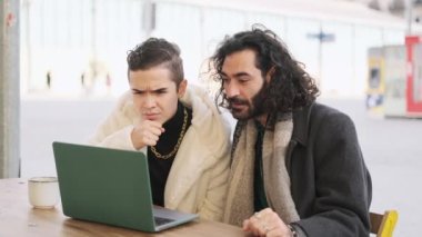 Slow motion video of a Gay couple using a laptop and suddenly raising the arms to celebrate something in a cafeteria