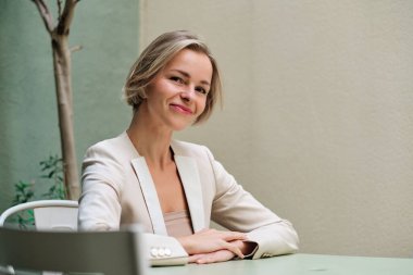 Businesswoman looking at camera and smiling while sitting on a table. Business and success concept.