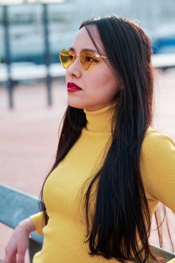 Woman with heart-shaped sunglasses looking away while standing outdoors.