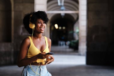 Young woman smiling while enjoying listening music with mobile phone and headphones outdoors. Technology concept.