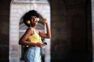 Happy woman looking at the camera and smiling while listening to music with headphones outdoors. Technology concept.