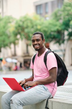 Man looking at camera and smiling while using a laptop outdoors. Technology concept.